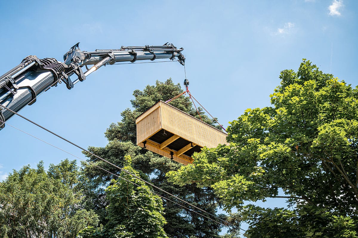 Crane lifting a prefabricated timber module above the treetops
