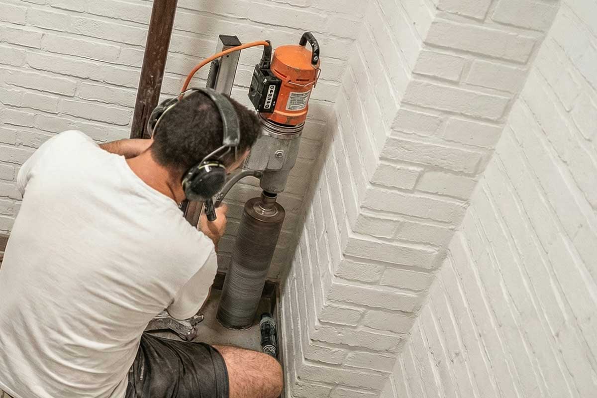 Worker with ear protection core-drilling through white-painted brickwork
